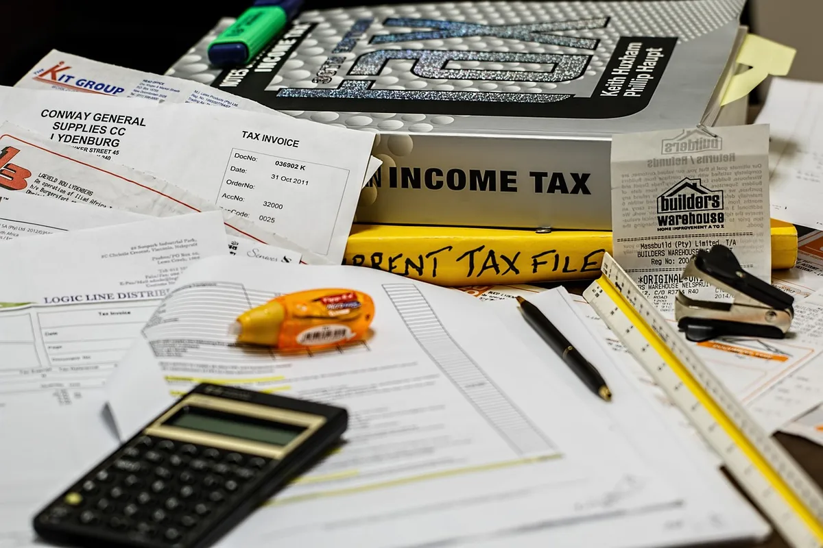 Table de cuisine avec documents fiscaux et calculatrice, mains anonymes feuilletant des papiers